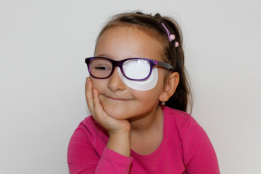 Portrait of a little girl who is wearing an eyepatch to correct her vision, Girl with glasses and eyepatch