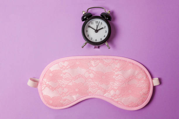 istock Sleeping mask and alarm clock on purple violet background 1144872736