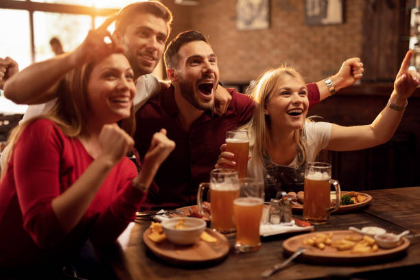 glückliche freunde jubeln für ihr team beim fernsehen im fernsehen in einer bar. - friendly match stock-fotos und bilder