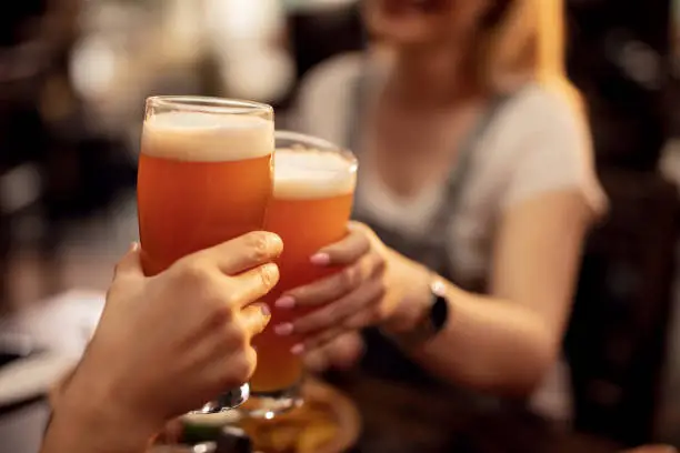 Close up of unrecognizable couple toasting with lager beer in a bar.