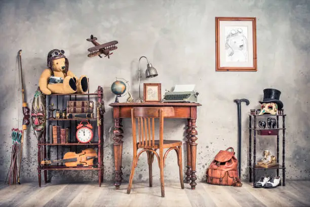 Photo of Vintage old typewriter, lamp, frame, forefinger on antique table, chair, Teddy Bear with photo camera, retro clock, books, fiddle, keys on shelf, plane, mask, cylinder hat, shoes, cane, backpack, bow