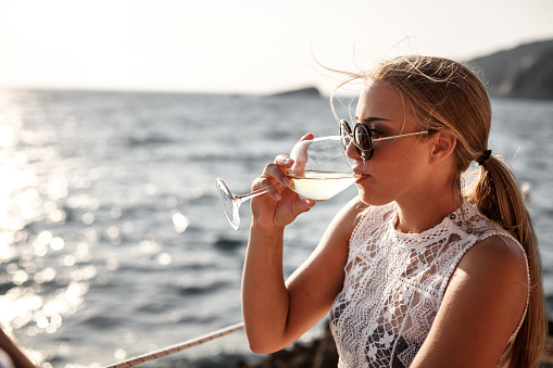 Side view of a young woman drinking white wine by the sea on a sunny day.