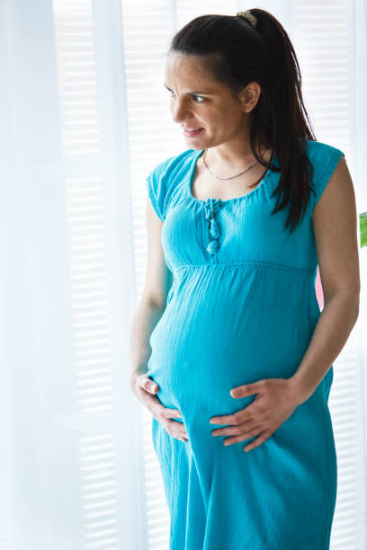 istock Woman touching her pregnant belly, looking through window 1144943498