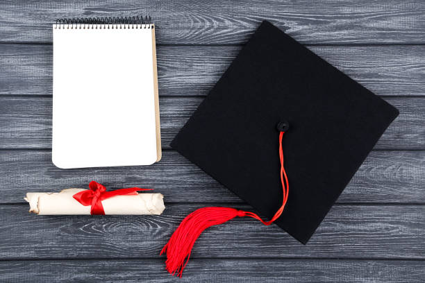 istock Graduation cap with diploma and notepad on black wooden table 1144948965