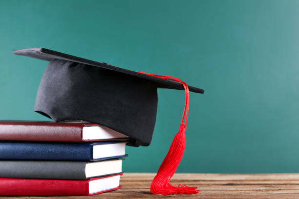 istock Graduation cap with stack of books on green board background 1144949521