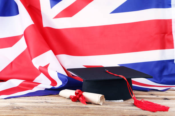 istock Graduation cap with diploma and British flag on brown wooden table 1144949647