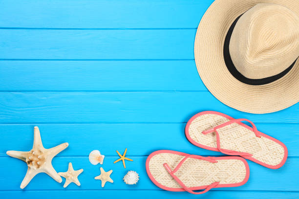 istock Pair of flip flops with seashells and hat on blue wooden table 1144950876