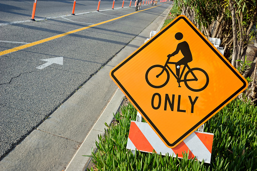 Side of the road has bicycle lane mark and cone off to oncoming cars. This Bicycle sign is also on side of the road for communication awareness and traffic management in Los Angeles.