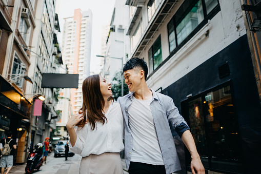 Young Asian couple smiling and embracing as they walk through local city street in Hong Kong