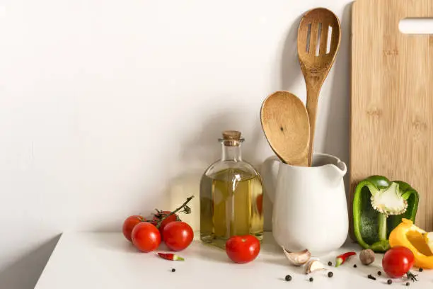 Photo of Wooden Kitchenware, olive oil and vegetables on table wall background. Template for text