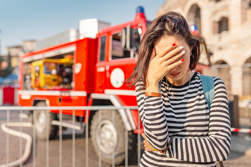 A woman in stress covers her face with her hands on the background of a fire fighting truck. Accident and insurance concept