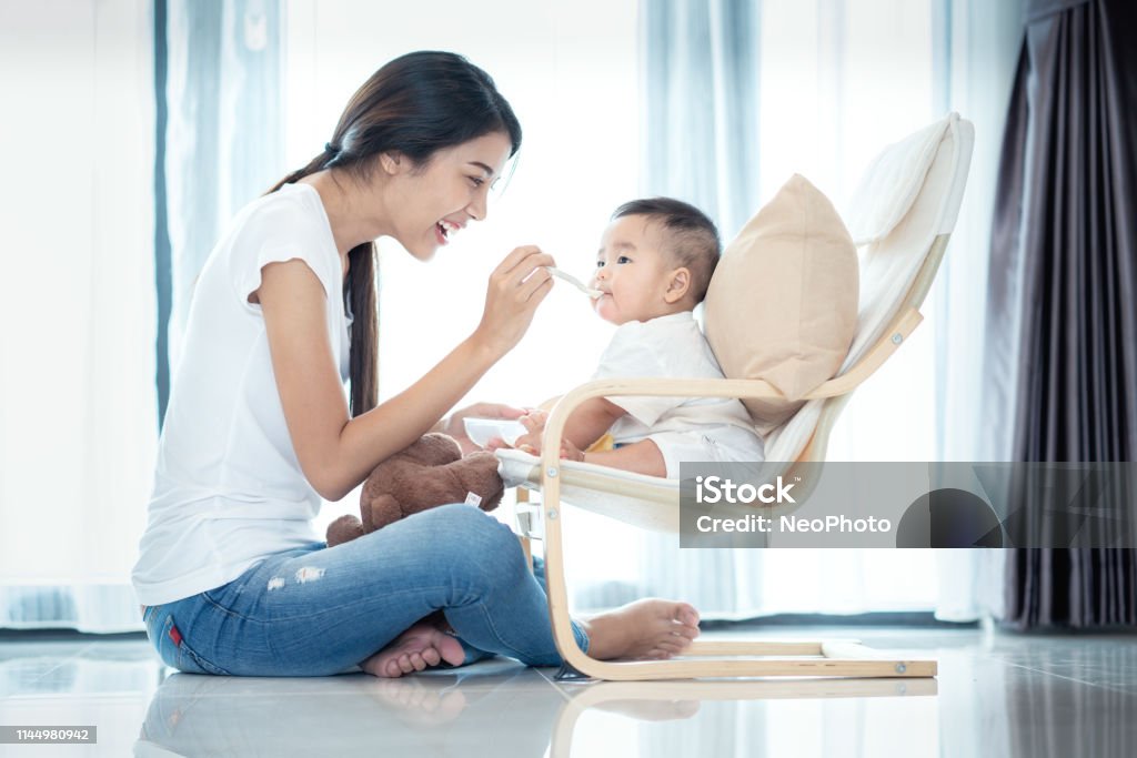 Asian mother feeding to her baby Asian mother feeding to her baby in leving room Baby - Human Age Stock Photo