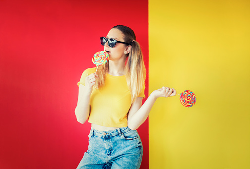 Portrait of beautiful young woman with fashion clothes and lollipop on mixed color background red&yellow.