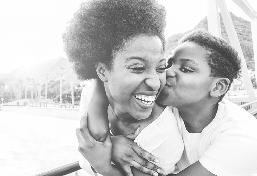 Happy young mother having fun with her child in summer day - Son kissing his mum outdoor - Family lifestyle, motherhood, love and tender moments concept - Focus on woman face - Black and white filter