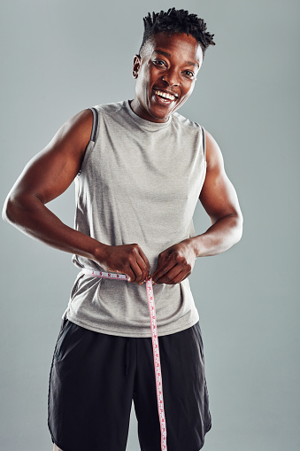 Shot of a sporty young man measuring his waist against a grey background