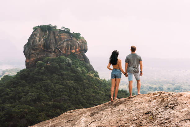 A couple in love on a rock admires the beautiful views. Boy and girl on the rock. A couple in love travels. Couple in Sri Lanka. Honeymoon in Asia. Man and woman in Sigiriya. Rear view pair stock photo