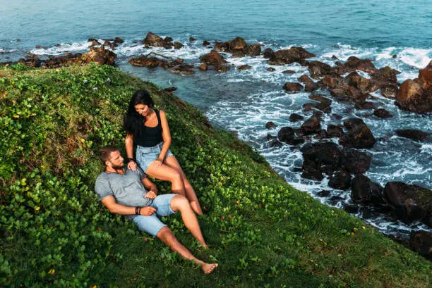 Photo of Couple on the shore of the sea meets the dawn. Man and woman on the coast. Lovers meet the sunrise at the sea. Honeymoon trip. Man and woman by the sea. Couple travels in Asia. A lonely pair. Lovers