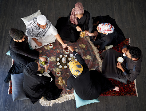 High angle shot of a group of young muslim friends having tea and treats at a gathering indoors
