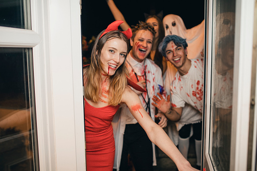 Group of friends dressed up in costumes laughing and having fun as they arrive at a Halloween party.