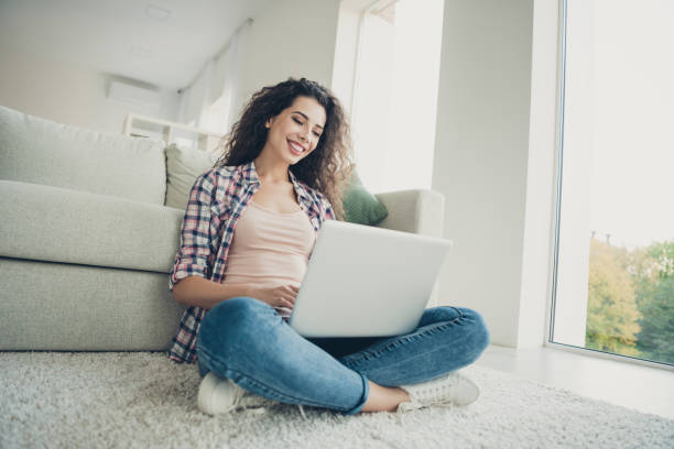 istock Portrait charming satisfied student youth use user device pc wireless connection conversation video call check news feed social network sit  lotus position plaid shirt jeans apartment 1144998187