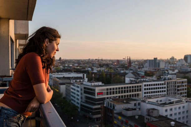 portrait de jeune femme se penche sur le balcon et regarde sur l’horizon de berlin tandis que le coucher du soleil - german culture people women germany photos et images de collection