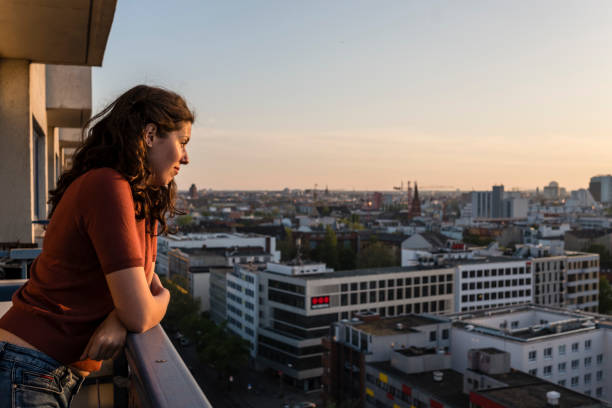 портрет молодой женщины наклоняется на балконе и смотрит на горизонт берлина во время заката - german culture people women germany стоковые фото и изображения
