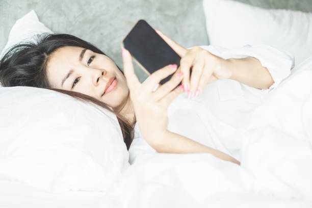 istock Asian woman laying down on bed hand using smart phone 1145001284
