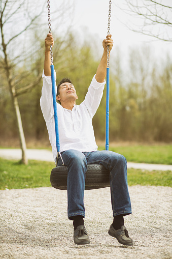 Japanese man sitting on a tire swing in a public park. Daydreaming with eyes closed.