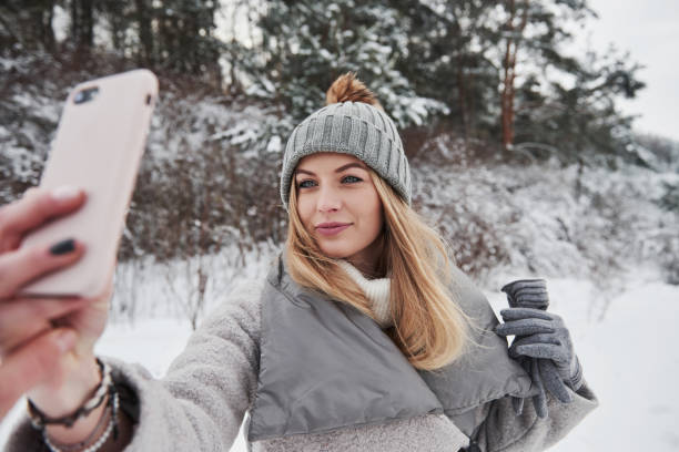 donna che scatta selfie all'aperto vicino alla foresta durante la giornata invernale innevata - snow heat adult blond hair foto e immagini stock