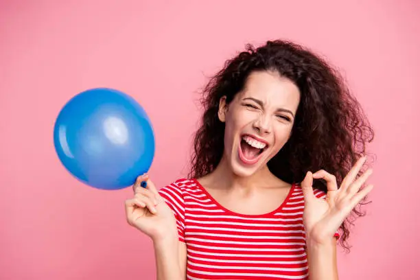 Close-up portrait of her she nice-looking attractive charming lovely crazy cheerful cheery wavy-haired lady holding in hand blue ball showing ok-sign isolated over pink pastel background