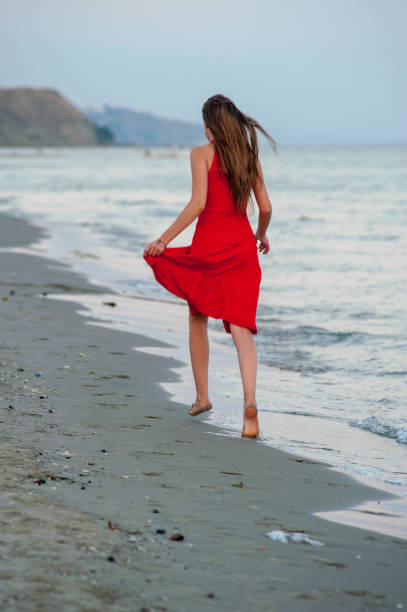 istock Young woman in red is running on the beach 1145014779