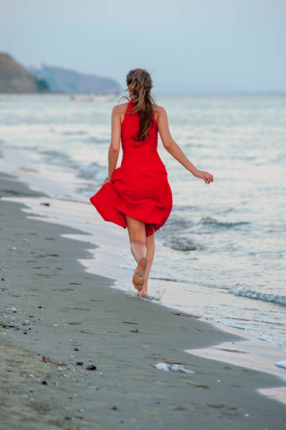 istock Young woman in red is running on the beach 1145014887