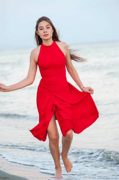 istock Young woman in red is running on the beach 1145015009