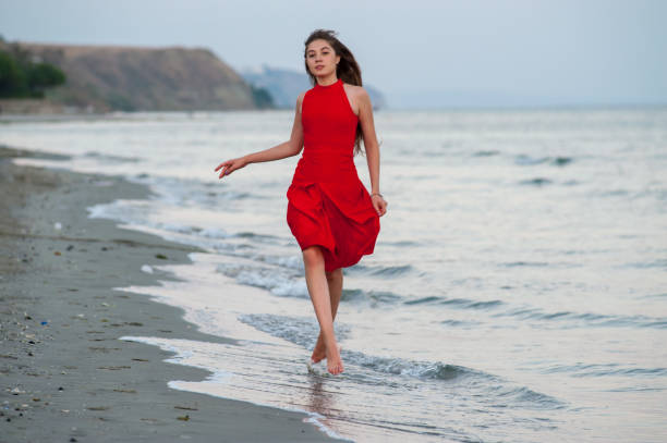 istock Young woman in red is running on the beach 1145015013