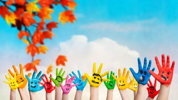 Photo of many colored hands with smileys in front of an autumn background