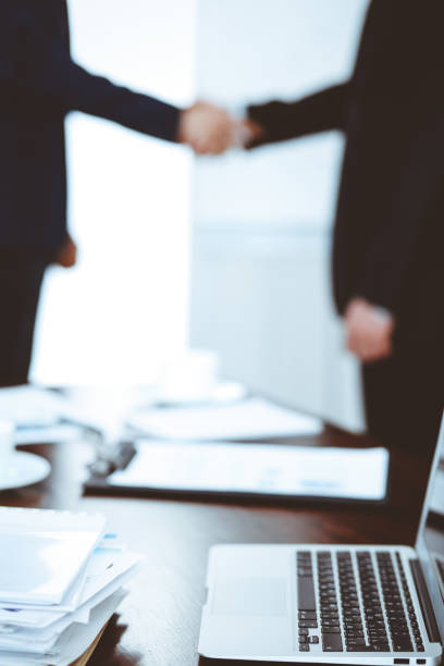 istock Documents and laptop on the table. Business people shaking hands on the background. 1145017981