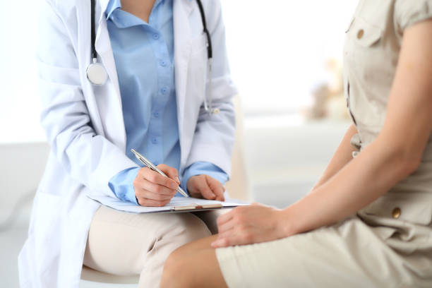 doctor and patient talking. physician at work in hospital while writing up medication history records form on clipboard near sitting woman. healthcare and medicine concepts. - medical exam doctor patient adult imagens e fotografias de stock