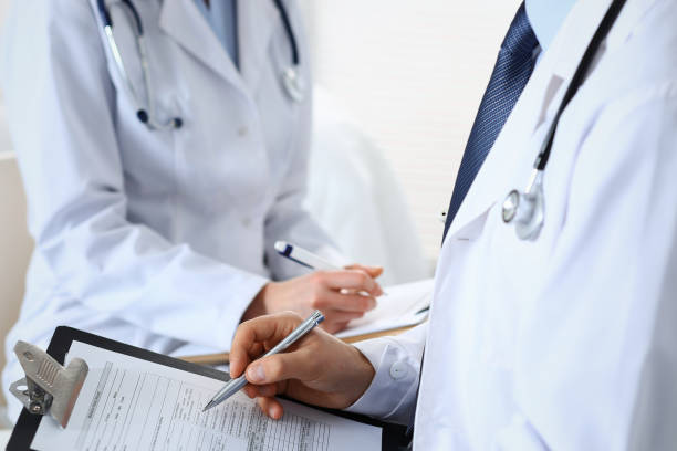 istock Two unknown doctors filling up medical form on clipboard, just hands closeup. Physicians asking question to patient or discussing medication program. Healthcare, insurance and medicine concept. 1145018346
