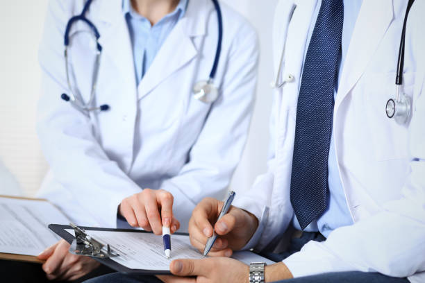 istock Two unknown doctors filling up medical form on clipboard, just hands closeup. Physicians asking question to patient or discussing medication program. Healthcare, insurance and medicine concept. 1145018363