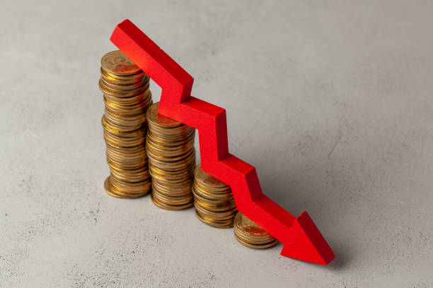 istock Green arrow down over stack of coins by ladder on gray background. 1145022600