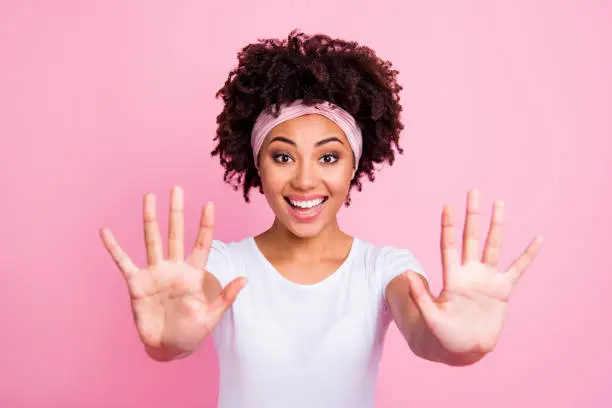 Close up photo beautiful amazing she her dark skin lady hold hands arms excited funky mood ten fingers show price without words wear head scarf casual white t-shirt isolated pink bright background.