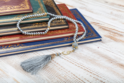 Holy Quran with arabic calligraphy meaning of Al Quran and tasbih or rosary beads over on wooden table. Selective focus and crop fragment.
