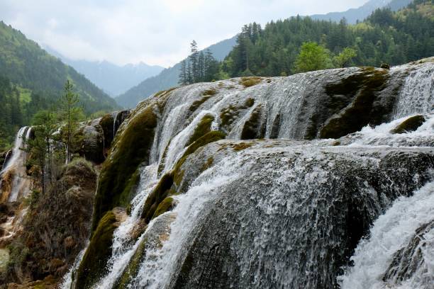 istock transparent waterfall splash falling down. green forest mountains and blue sunny sky. 1145030649