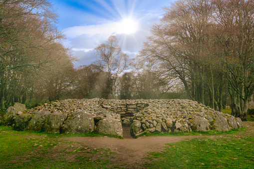 Clava cairns are a collection of over fifty Bronze Age Standing Stones.  Here we see a circular chamber tomb cairn, with sun rays above.  The site aligns with the Winter Solstice.  They are located to the east of Inverness in Scotland, UK.  The public have a free right of access to the site.