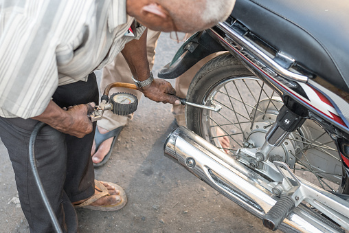 Phnom Penh, Cambodia - January 28, 2019: an old man inflates a motorbike tire in the street. Tire inflation is a business for many people who stands with the equipment in street waiting for a client.