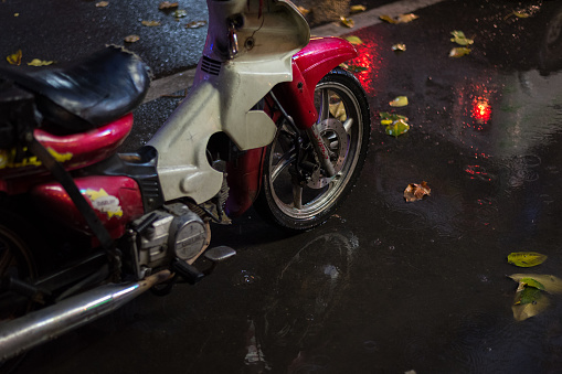 Phnom Penh, Cambodia - January 17, 2019: a motorbike stands on the night street in the rain, in the puddle with wet fallen leaves.