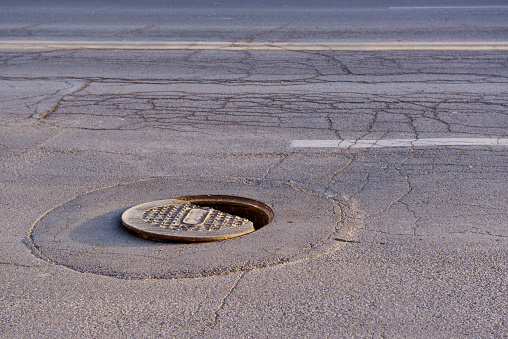 Broken iron manhole cover dangerously open in the middle of the street.