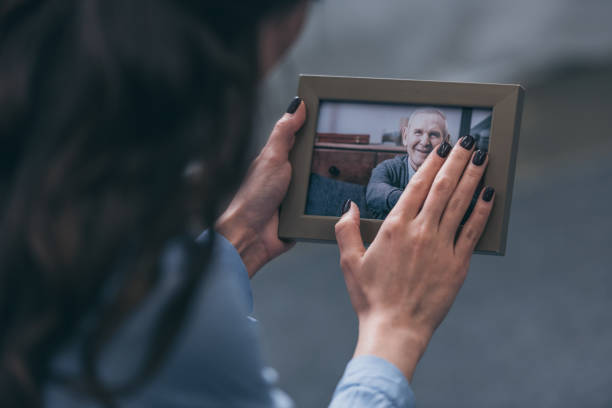 cropped view of woman holding photo frame with mature man at home, grieving disorder concept cropped view of woman holding photo frame with mature man at home, grieving disorder concept holding photos stock pictures, royalty-free photos & images