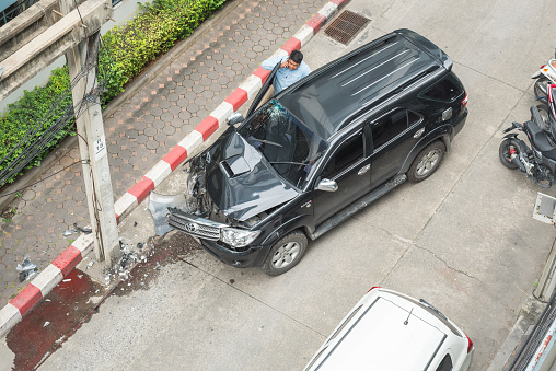 Bangkok, Thailand - December 12, 2018: a car owner makes a call after crashing his car against a power pole in an empty backstreet.