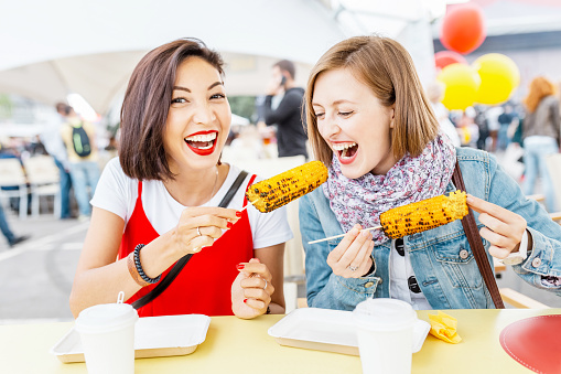 Woman friends eating street food corn at fastfood festival